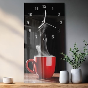 Op de afbeelding: Rechthoekige wandklok met een rode koffiemok en opstijgende stoom tegen een donkere achtergrond. De klok heeft witte cijfers en wijzers. Deze decoratieve klok past in een keuken of eetkamer.