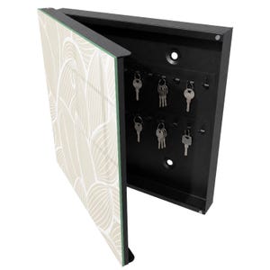 Può includere: Un armadietto portachiavi da parete nero con lo sportello aperto caratterizzato da un motivo astratto a foglie beige e bianco. L'interno è in metallo nero con due file orizzontali di ganci, che ospitano cinque chiavi in metallo argentato.