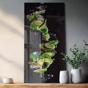 May include: A rectangular wall clock featuring a vertical graphic of sliced limes, green mint leaves, and splashing water against a dark background. The clock face includes thin black hands and minimalist hour markers printed directly on the glass surface.