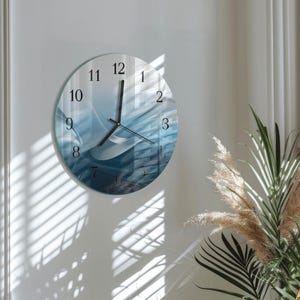 May include: A round wall clock with a blue and white abstract design. The clock face features black numerals and hands. The clock is mounted on a white wall, with shadows from a window visible.