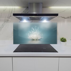 May include: A white lotus flower with sparkling lights behind it, reflected in a blue water surface. The image is on a glass backsplash behind a black stovetop.