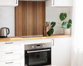 May include: A kitchen featuring white cabinets, a stainless steel oven, and a silver kettle. The backsplash consists of vertical wood slats in varying brown tones. A green monstera plant in a light-colored pot sits on the wooden countertop.