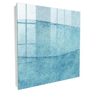 Può includere: Un pannello artistico da parete quadrato in vetro con un design astratto a strati in varie tonalità di blu. La superficie ha una finitura lucida e riflettente con un aspetto strutturato, che mostra bande orizzontali di toni blu chiaro, medio e scuro.