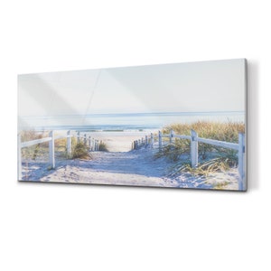 May include: A white wooden fence lines a sandy path leading to a beach with blue water and white waves.