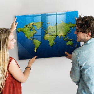 以下が含まれることがあります： 白い壁に世界地図を掛けているカップル。地図は青い背景と緑色の大陸が描かれた透明なアクリルパネルに印刷されています。