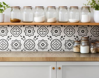 May include: A kitchen scene featuring a wooden shelf holding seven clear glass jars with wooden lids, filled with various ingredients. Below the shelf, a backsplash displays a repeating black and white geometric tile pattern above light gray cabinets.