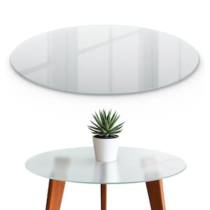 May include: A clear, oval glass tabletop is shown above a small, round glass table with wooden legs. A small potted succulent plant sits on the table. The table is a modern design.