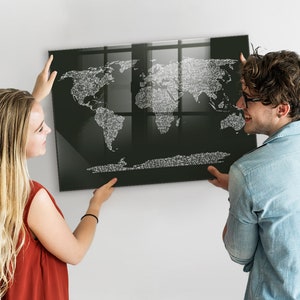以下が含まれることがあります： 2 人の人が白い壁に黒い世界地図をかけています。地図は白い文字でできており、黒い額縁に入っています。