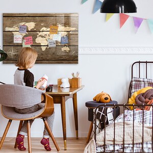 以下が含まれることがあります： 子供部屋の壁に、付箋が付いた木製の世界地図が飾られています。地図には羅針盤のデザインがあります。子供は緑色のデスクランプのある机に座っています。背景には枕と犬の形をした枕のあるベッドがあります。