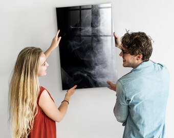 Puede incluir: Dos personas están colgando una impresión de arte abstracto en blanco y negro en una pared blanca. La impresión presenta un diseño de humo en espiral.