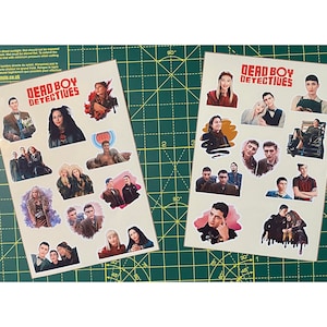 Può includere: Due fogli di adesivi con personaggi dello show televisivo "Dead Boy Detectives". Gli adesivi sono su un tappetino da taglio verde. Gli adesivi sono stampati su carta bianca con uno sfondo marrone chiaro. Gli adesivi presentano vari personaggi dello show, tra cui un giovane con i capelli castani e una camicia blu, una giovane donna con i capelli neri lunghi e una camicia nera, e un giovane con i capelli biondi e una camicia bianca.
