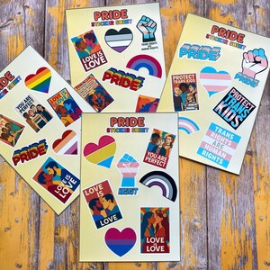 May include: Pride sticker sheets featuring various LGBTQ+ pride flags, hearts, and slogans like "Love is Love," "Protect Trans Kids," and "Trans Rights are Human Rights." The sheets are on a yellow background.