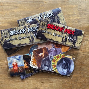 May include: A clear plastic bag filled with a variety of stickers. The stickers feature illustrations of occult, celestial, and creepy themes. The bag is labeled with the text "Sticker Pack Occult, Celestial & Creepy".