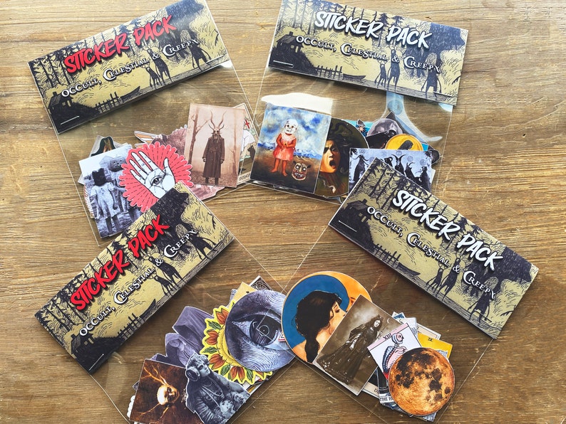 May include: Four clear plastic bags filled with sticker packs. Each bag has a sticker pack with a black and white illustration of a house in the woods with the text "Occult, Creepy & Creepy" on it. The stickers in the bags are various colors and feature illustrations of eyes, hands, faces, and other spooky imagery.