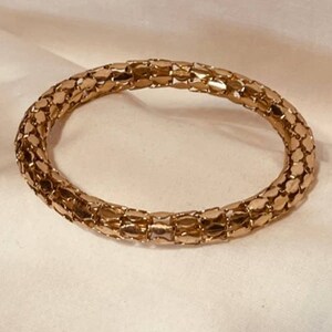 May include: A gold-toned chain bracelet with a woven design. The bracelet is made of small, interlocking links that create a flexible and comfortable fit.