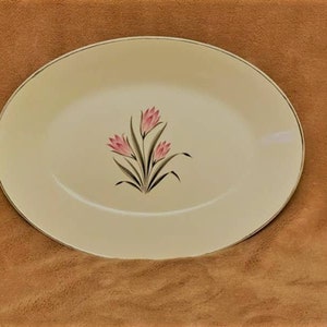May include: A white oval serving platter with a gold rim and a floral design featuring pink flowers and green leaves.