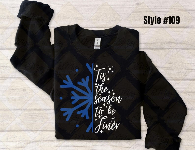 May include: Black sweatshirt with a blue snowflake design and the phrase "Tis the season to be Finer" in white script. The long-sleeved shirt has a crew neck and is a winter-themed apparel item.