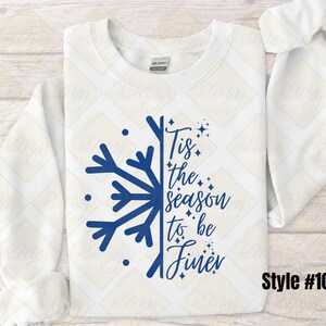 May include: A white sweatshirt with a blue snowflake design and the phrase "Tis the season to be finer." The design includes stars and dots. The style number is #107.
