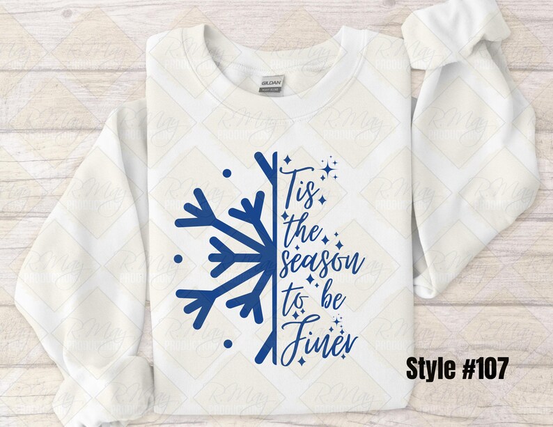 May include: A white sweatshirt with a blue snowflake design and the phrase "Tis the season to be finer." The design includes stars and dots. The style number is #107.