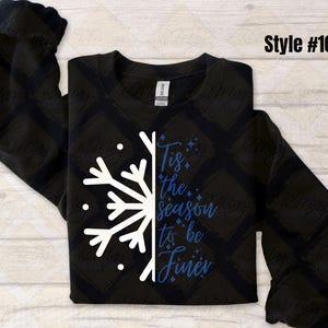 May include: Black sweatshirt with a white snowflake design on the left side and the phrase "Tis the season to be Finer" in blue script. The sweatshirt has long sleeves and a crew neck. Style #108 is printed in black.