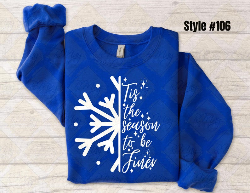 May include: Royal blue sweatshirt with a white snowflake design and the text "Tis the season to be finer." The long-sleeved top has a diamond pattern and rolled cuffs. Style #106 is printed in the upper right corner.