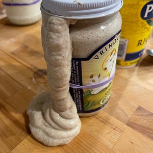 May include: A glass jar with a white lid filled with a thick, light brown substance. The substance is overflowing from the jar and has a smooth, creamy texture. The jar has a label with the text "VRINDA" and a picture of a goat. The text "For centuries in Asia, Ghor pure butter oil, the standard of excellence in cooking, Ghor's flavor is unmatched. That's why it's widely used by professional chefs." is also on the label.
