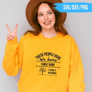 May include: A yellow sweatshirt with the text "THESE PEOPLE HERE are home FAMILY NAME FAMILY REUNION" in black. The sweatshirt has a crew neck and long sleeves. The image also includes a woman wearing a brown hat.
