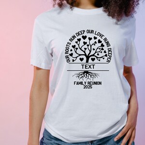 Op de afbeelding: Wit T-shirt met een zwart familiebomenontwerp. De boom heeft harten als bladeren en de tekst "Onze wortels lopen diep, onze liefde loopt dieper" cirkelt rond de boom. Onder de boom staat de tekst "Familiere&uuml;nie 2025".