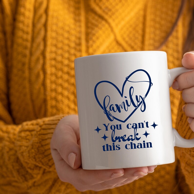 May include: White ceramic mug with a blue heart-shaped design that says "Family". Below the heart, the mug reads "You can't break this chain" in blue script. The mug has a white handle and is held by a person wearing a yellow sweater.