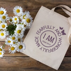 May include: A white canvas tote bag with a purple circle design that says "I AM FEARFULLY AND WONDERFULLY MADE. PSALM 139:14" with two butterflies on the right side of the circle.