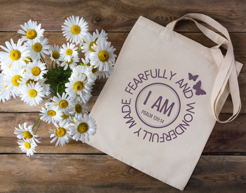 May include: A white canvas tote bag with a purple circle design that says "I AM FEARFULLY AND WONDERFULLY MADE. PSALM 139:14" with two butterflies on the right side of the circle.
