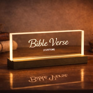 May include: A rectangular, illuminated sign with the words "Bible Verse" in elegant script. The sign is lit from within, casting a warm glow. The base is a dark wood, and the text reads "(CUSTOM)".