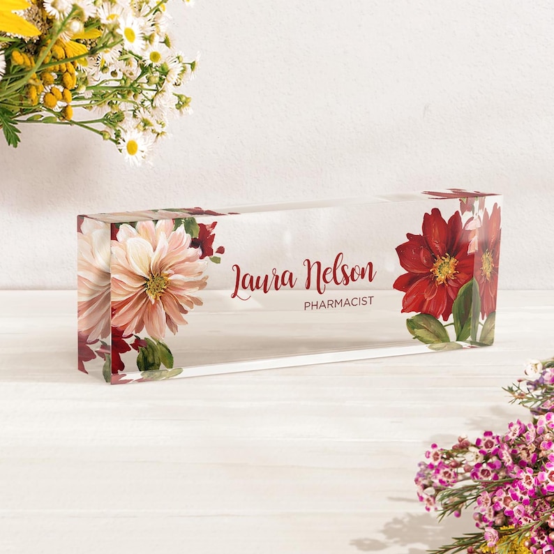 Peut inclure: Un porte-nom de bureau en acrylique transparent avec un motif floral compos&eacute; de fleurs rouges et roses. Le porte-nom indique "Laura Nelson, Pharmacienne".