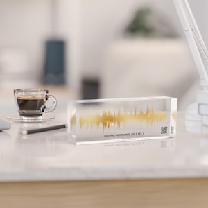 Könnte beinhalten: Ein transparenter Acrylblock mit einem goldenen Schallwellendesign im Inneren. Der Text "CHOPIN - NOCTURNE, OP. 9 NO. 2" ist auf der Unterseite des Blocks aufgedruckt.