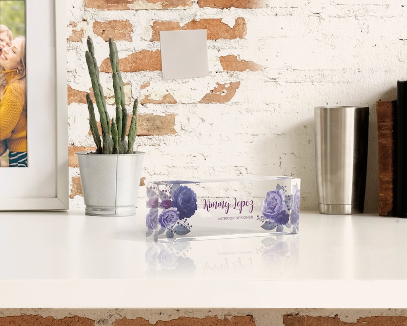 May include: A clear glass paperweight with a floral design and the text "Kimmy Lopez Interior Designer".