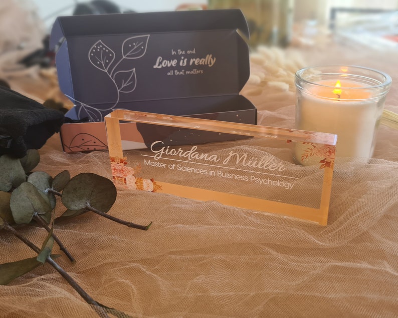 Peut inclure: Une plaque de nom de bureau en acrylique transparente avec un motif floral et le texte "Giordana M&uuml;ller, Master of Sciences in Business Psychology".