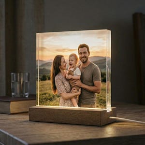 May include: A lighted photo block with a family portrait. The image is encased in a clear acrylic block, mounted on a wooden base. The family is smiling in a field with mountains in the background. The block is illuminated from within.