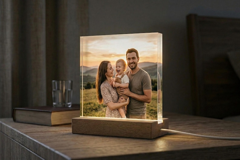 May include: A lighted photo block with a family portrait. The image is encased in a clear acrylic block, mounted on a wooden base. The family is smiling in a field with mountains in the background. The block is illuminated from within.