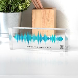May include: A clear acrylic block with a blue and green sound wave design inside. The text "MOZART - PIANO CONCERTO NO. 21" is printed on the bottom of the block. A QR code is printed on the right side of the block.