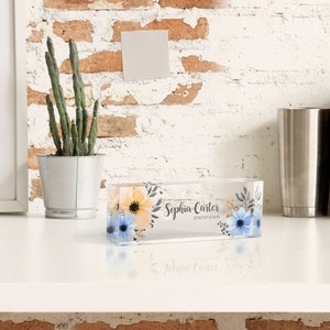 Peut inclure: Un bloc acrylique transparent avec un motif floral et le texte "Sophia Carter, Statistician". Le bloc est pos&eacute; sur une surface blanche.