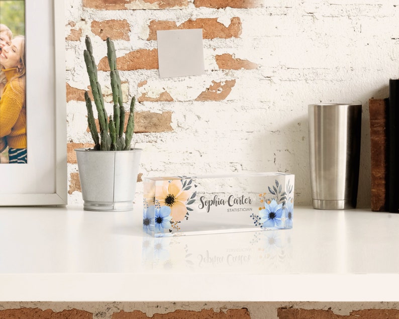 Peut inclure: Un bloc acrylique transparent avec un motif floral et le texte "Sophia Carter, Statistician". Le bloc est pos&eacute; sur une surface blanche.