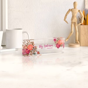 May include: A clear acrylic desk nameplate with a floral design and the text "Lily Anderson Teacher".