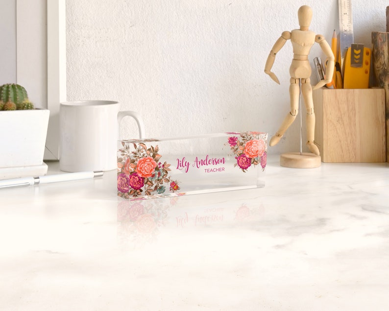 Peut inclure: Un porte-nom de bureau en acrylique transparent avec un motif floral et le texte "Lily Anderson Teacher".