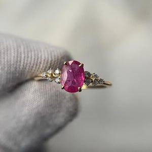 Puede incluir: Un anillo de oro con una gran gema rosa de corte ovalado como pieza central. Pequeñas gemas claras están engastadas a ambos lados de la piedra principal. El anillo tiene un diseño delicado y elegante.