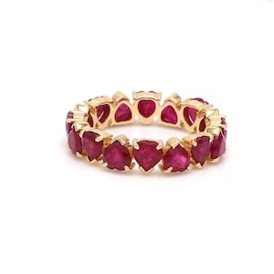 Könnte beinhalten: Ein goldener Eternity-Ring mit einer durchgehenden Reihe leuchtend roter, herzförmiger Edelsteine, die in polierte Gelbgoldfassungen eingefasst sind. Der Ring zeigt ein sich wiederholendes Muster aus facettierten Rubinen in einem Kreis.