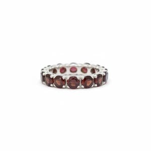 May include: A silver eternity band ring featuring a continuous row of round, deep red garnet gemstones set in individual metal prongs. The ring displays a uniform circular design with polished silver metal visible between each faceted stone.