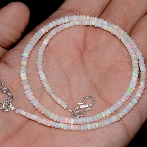 May include: A delicate necklace composed of small, white opal beads with iridescent flashes of color. The necklace is strung on a fine chain and features a silver-colored clasp. The beads are round and vary slightly in size.