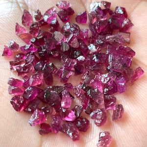 May include: A collection of loose pink and purple gemstones, likely rubies or sapphires, in various shapes and sizes. The gemstones are scattered on a hand, showcasing their natural beauty and brilliance.