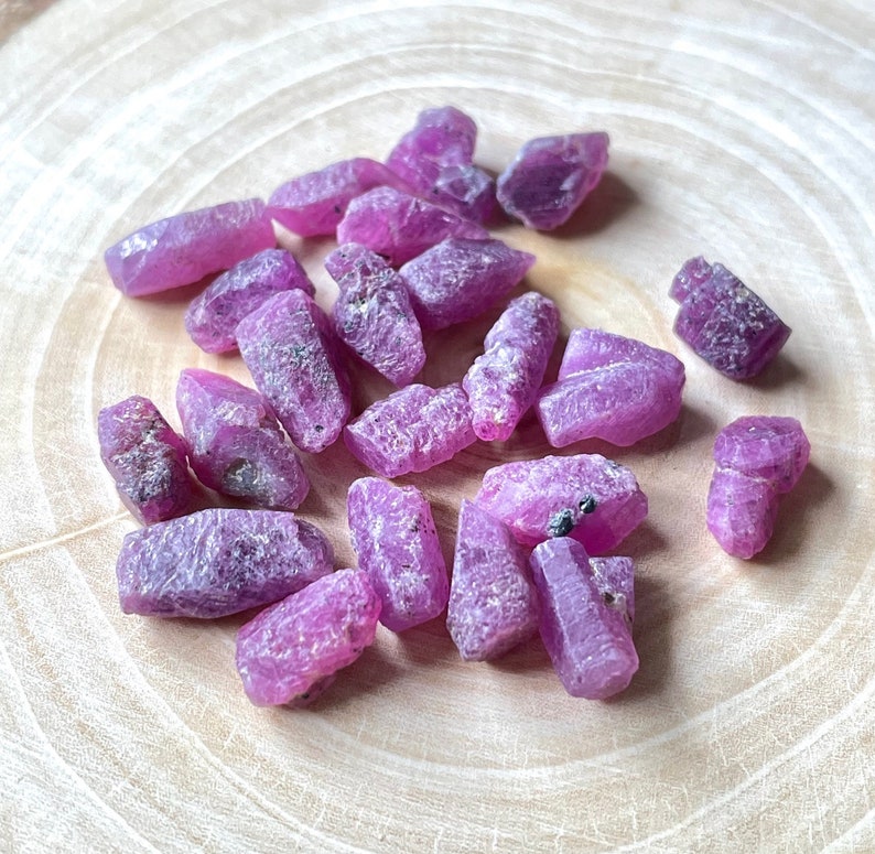 Pu&ograve; includere: Una collezione di cristalli grezzi di rubino rosa, di varie forme e dimensioni, esposti su una superficie di legno.