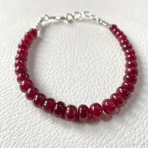 Op de afbeelding: Een armband van rode edelstenen met een zilveren sluiting. De armband is gemaakt van ronde, gladde kralen.